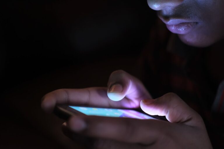 Руки набирают сообщение на светящемся экране телефона в темноте